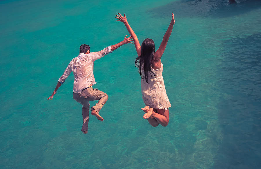 Happiness jump of young couple on the water. Retro style color tones.