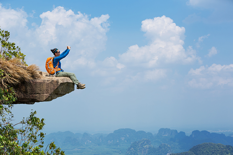 successful woman hiker taking photo with smartphone on mountain peak cliff
