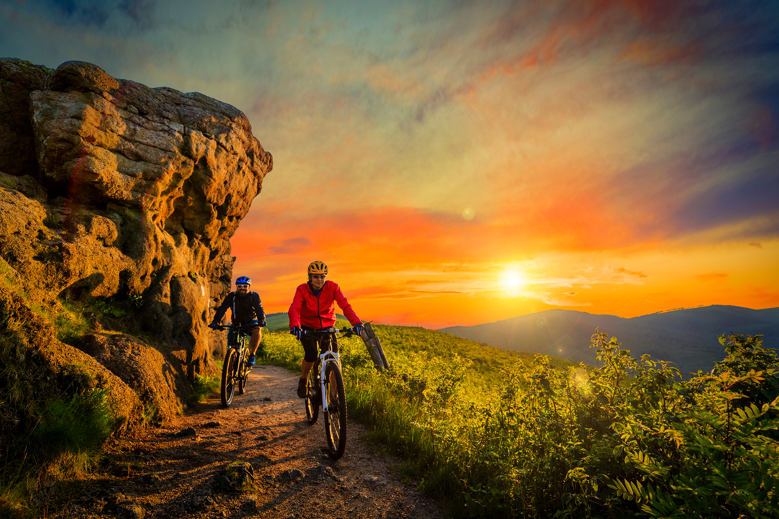 Mountain biking women and man riding on bikes at sunset mountains forest landscape. Couple cycling MTB enduro flow trail track. Outdoor sport activity.